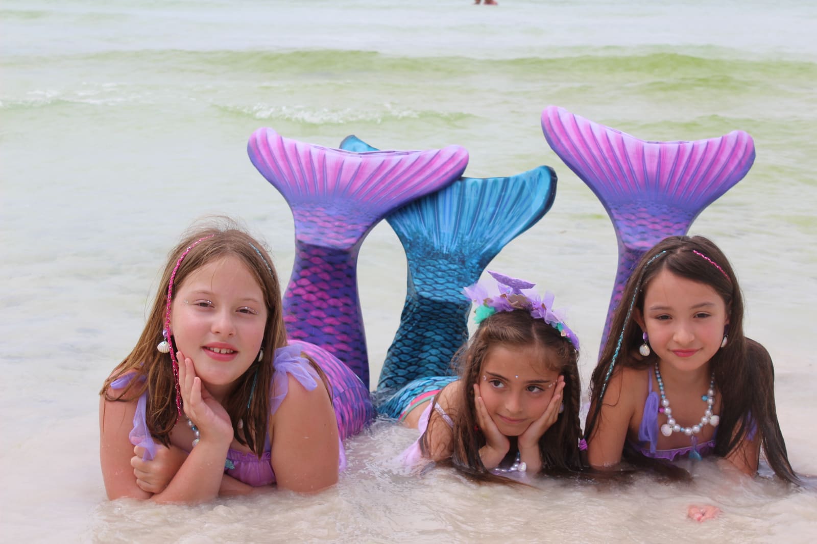 Three young mermaids in colourful tails posing on Boracay's white sand at the water's edge